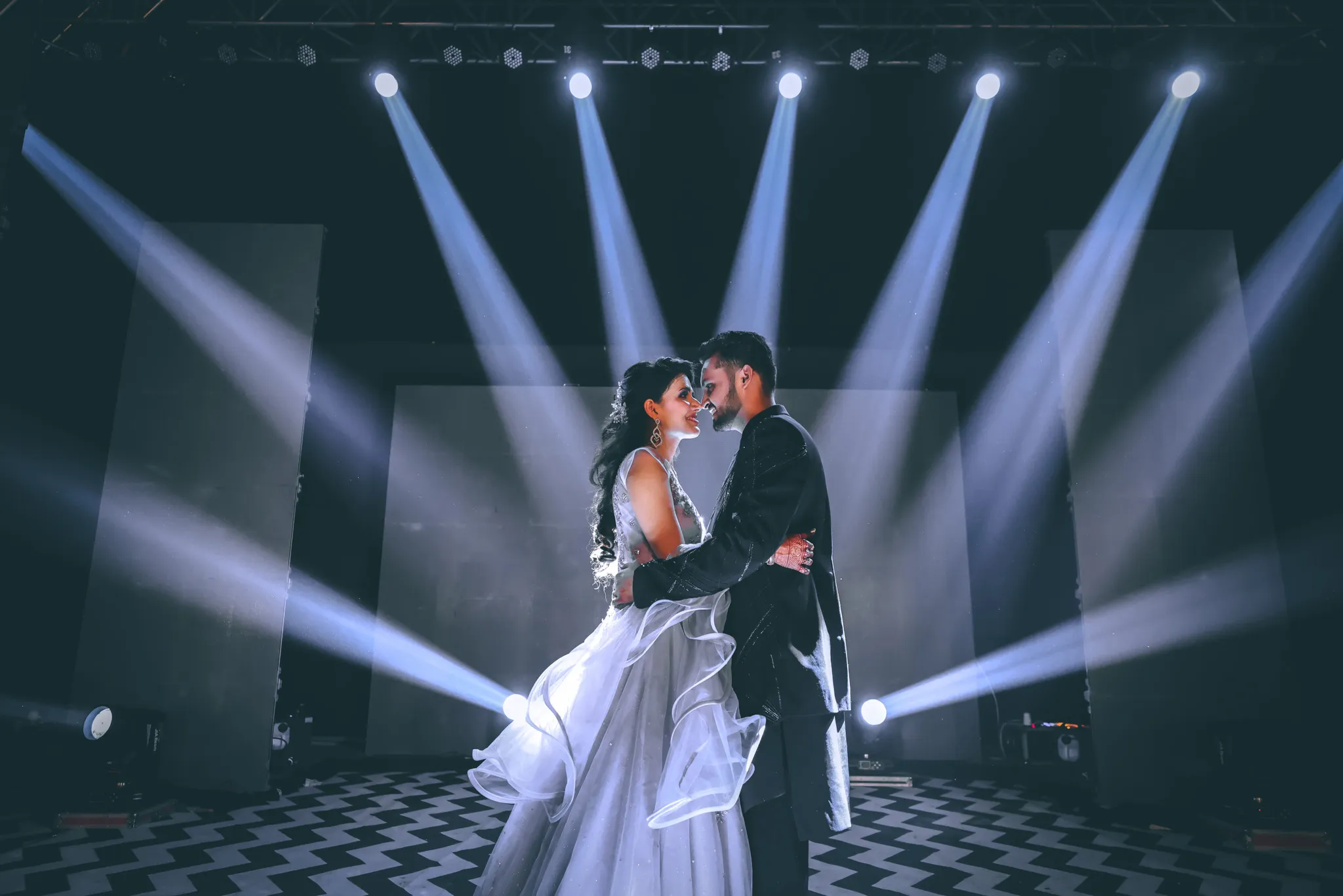 Couple dancing under spotlight during wedding photoshoot with dramatic lighting.