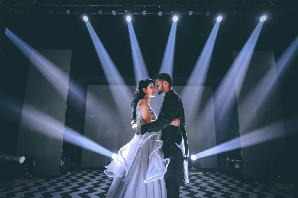 Couple dancing under spotlight during wedding photoshoot with dramatic lighting.